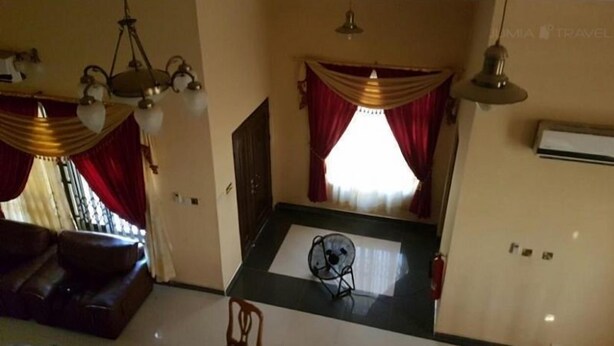 A living room with a sofa, a dining table with a fan, and a window with red curtains. - Huford  Lodge (Oyibi)