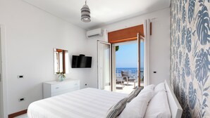Ein Schlafzimmer mit einem großen Bett, einem Fernseher, einem Schminktisch und Meerblick durch eine offene Tür.