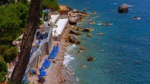 Ein Küstenhotel mit einer Steinstufe, die zu einer Terrasse führt, klarem blauen Wasser und einer felsigen Küste.