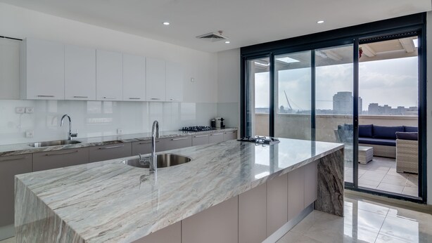 A modern kitchen with a large island, a sink, and a view of the city through large windows. - Jerusalem Penthouse (Jerusalem)
