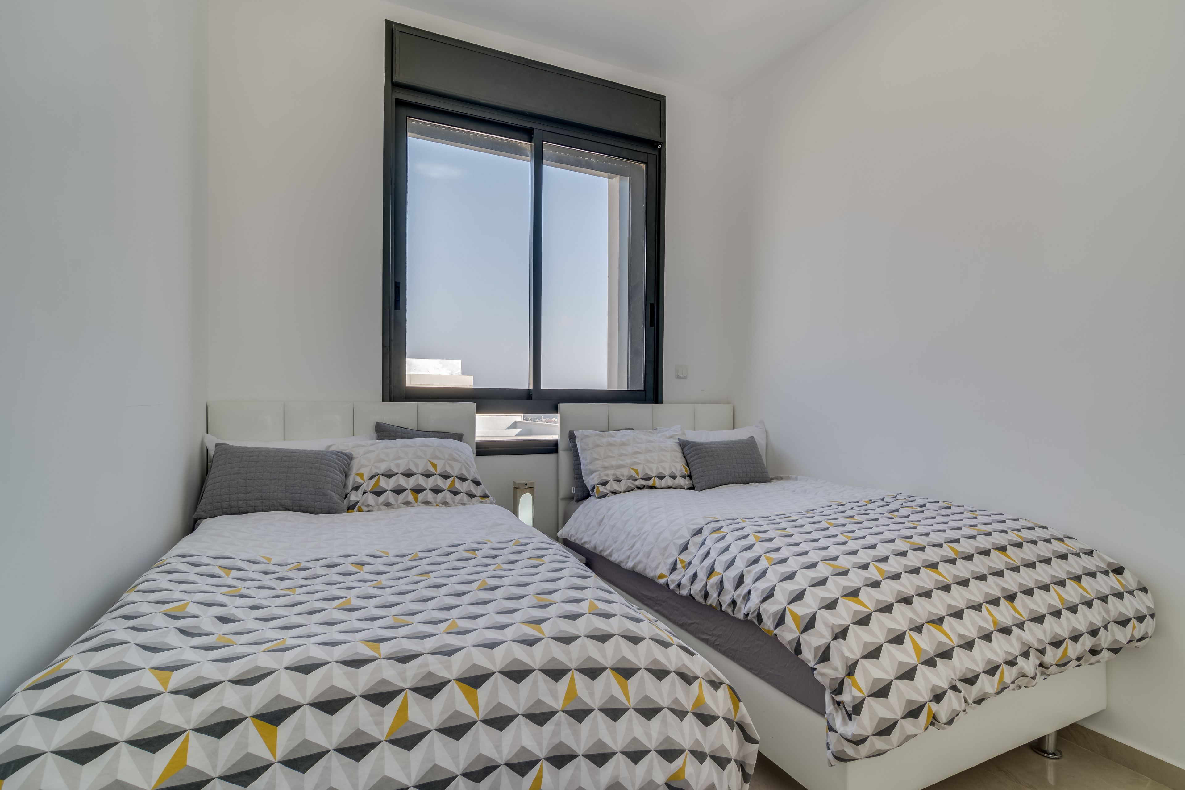 A bedroom with two beds, a window, and a white headboard.