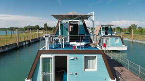 Una casa flotante con terraza, un bote pequeño y un espacio cubierto.