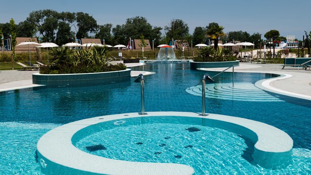Una piscina de diseño circular, rodeada de sillones de descanso y sombrillas.