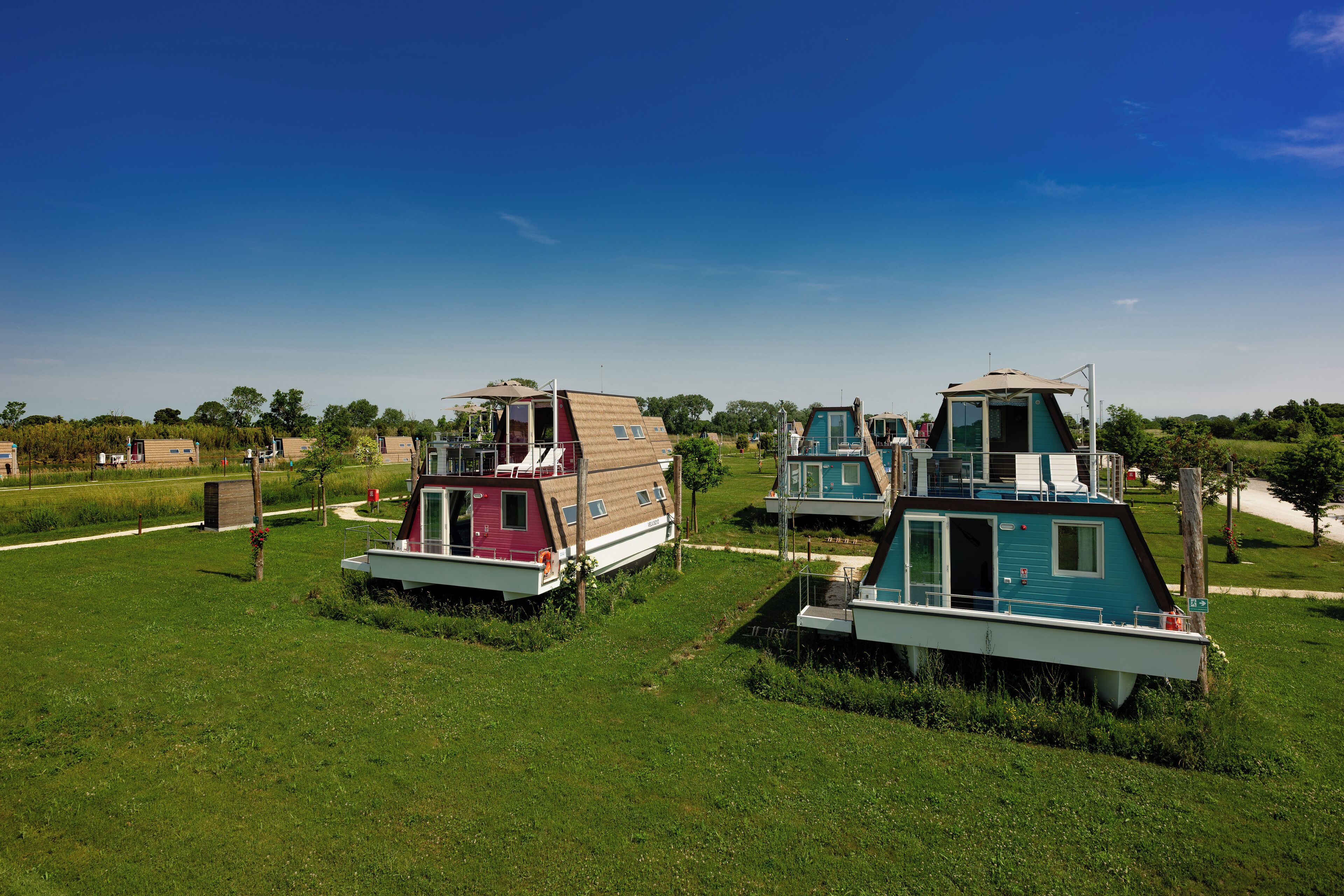 Two floating houses with open decks and a grassy area in the foreground.