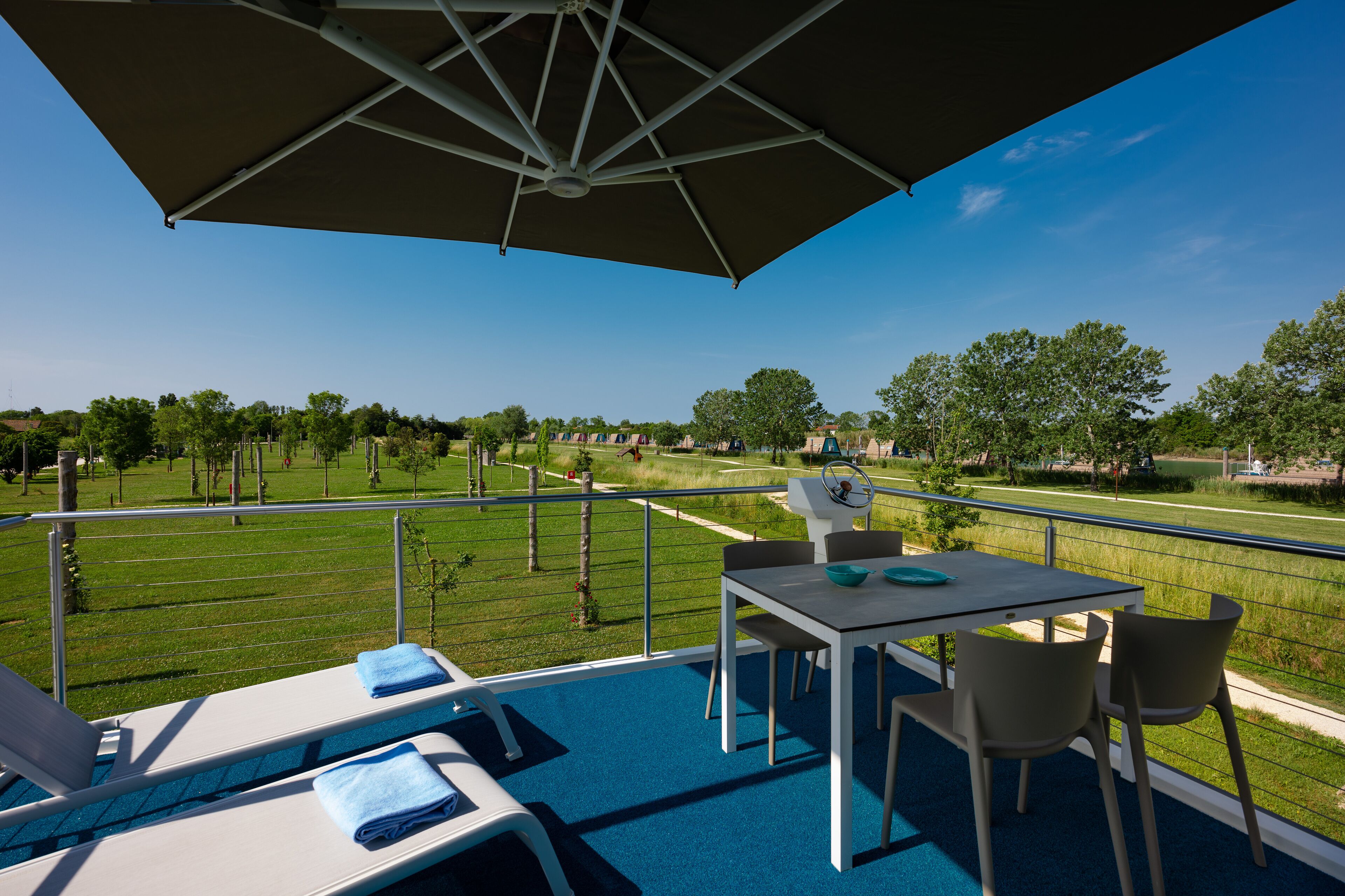 A balcony with a pool, a table, chairs, and a view of a park.