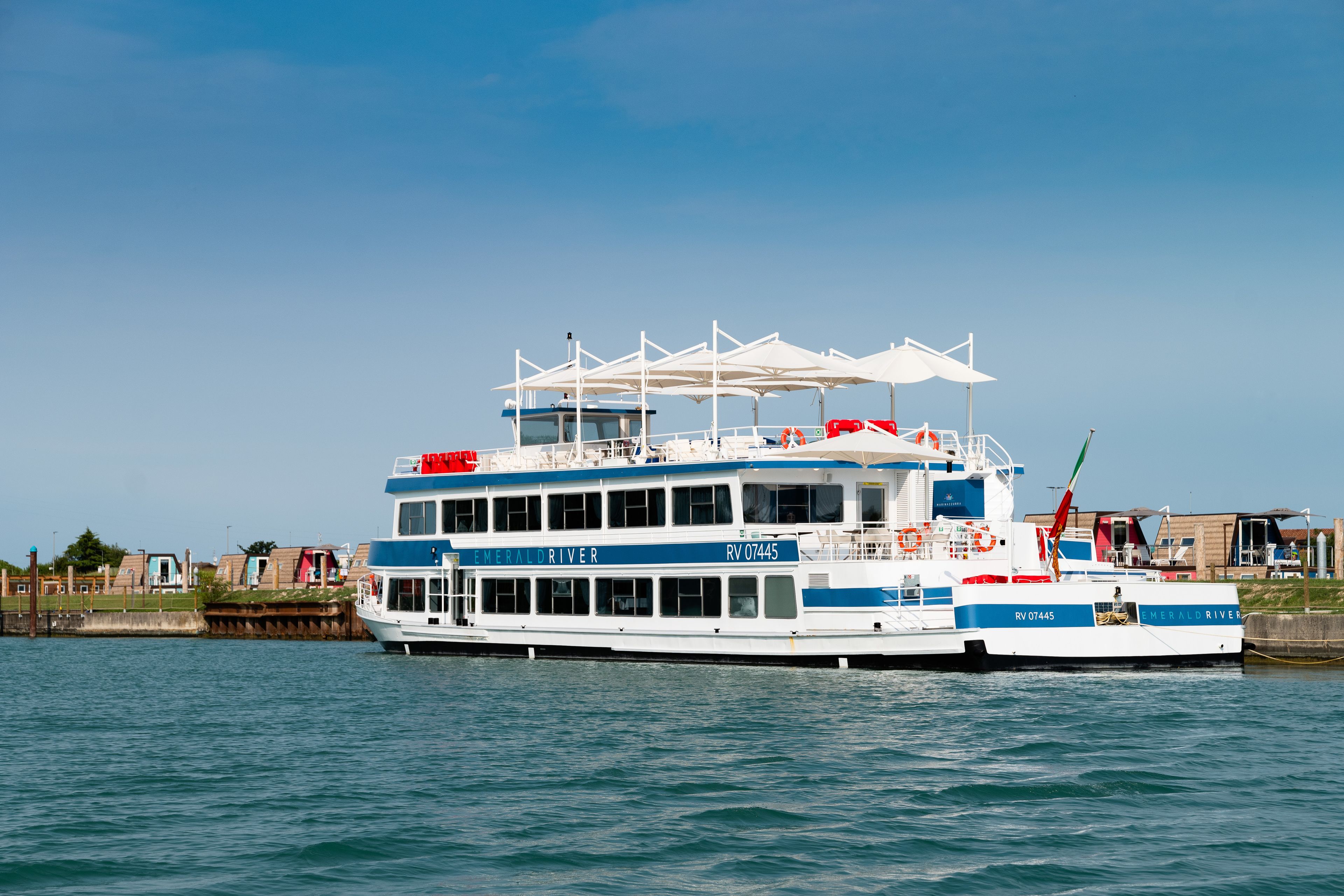 A large, multi-deck river cruise ship with "Emerald Driver" written on the side, docked at a pier with buildings in the background.
