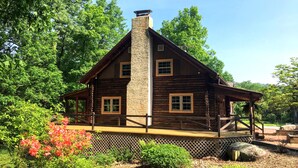 A log cabin with a stone chimney, wooden deck, and surrounded by lush greenery. - Fox Creek Cabin in the woods with stream (Narvon)