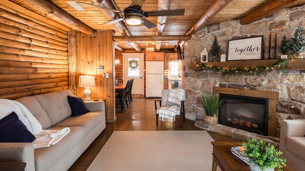 A cozy log cabin interior with a fireplace, a sofa, a dining area, and a kitchen. - Fox Creek Cabin in the woods with stream (Narvon)