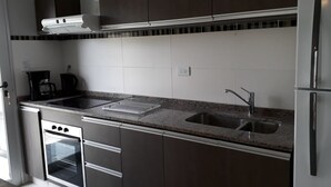 A modern kitchen with dark cabinets, a double sink, a built-in oven, and a stainless steel refrigerator. - DUPLEX LA PUNTILLA (Chacras de Coria)