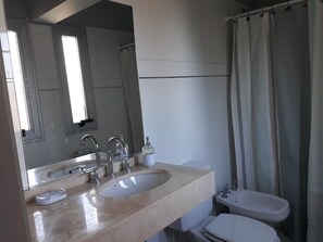 Un baño con lavamanos doble, inodoro, ducha con cortina y un espejo grande.