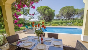 Un área de comedor al aire libre con vista a la piscina, mesas dispuestas con vajilla blanca y sillas verdes.
