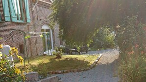A gravel pathway leading to a brick building with a garden area. - Les Chambres du Relais (Liettres)