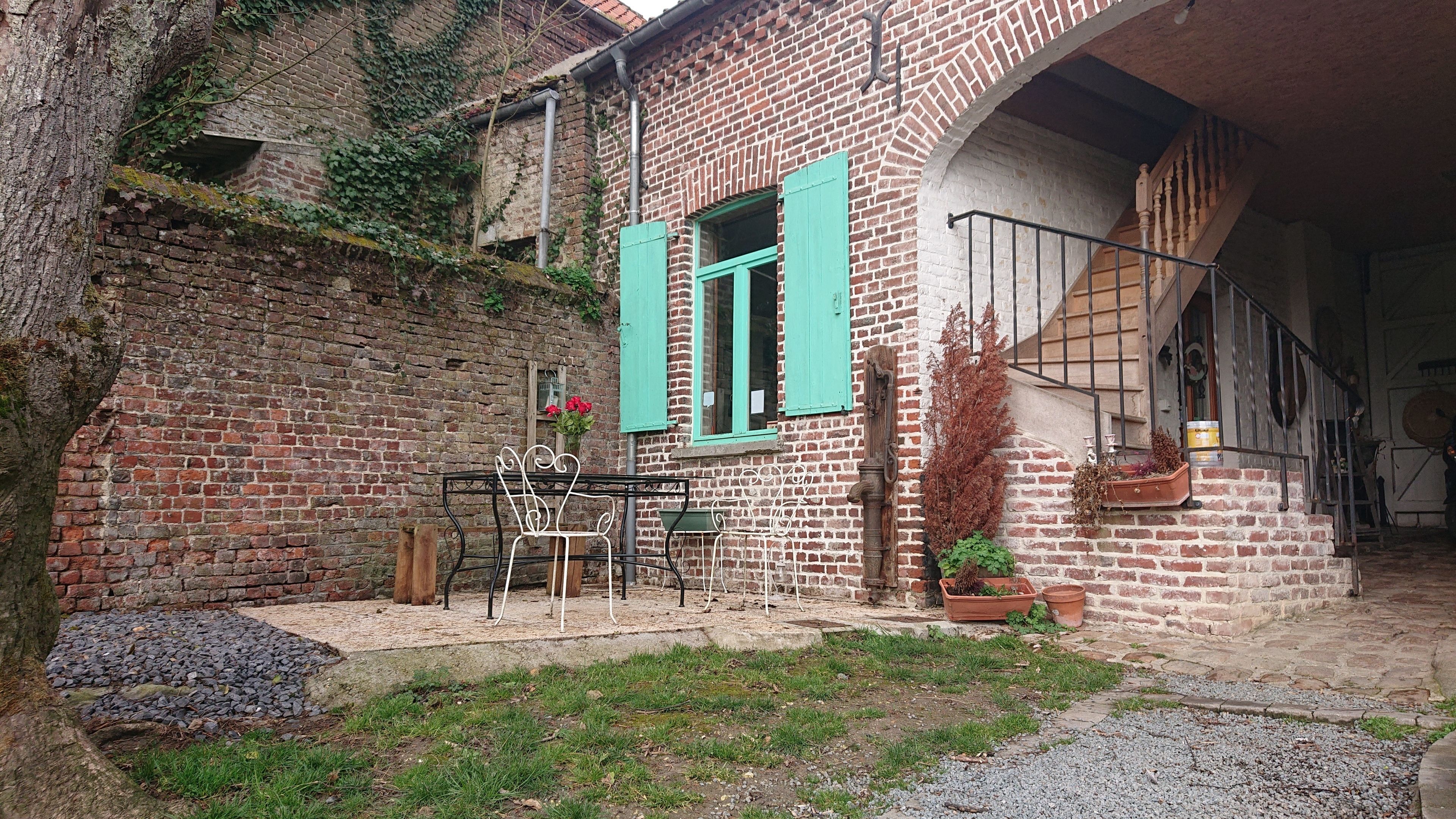 A rustic courtyard with a brick building, a wooden bench, and potted plants.
