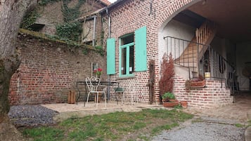 A rustic courtyard with a brick building, a wooden bench, and potted plants.