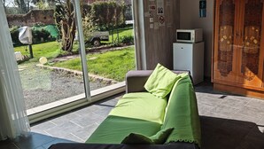 A room with a bed, a small white refrigerator, a wooden cabinet, and a view of a garden and street outside. - Les Chambres du Relais (Liettres)
