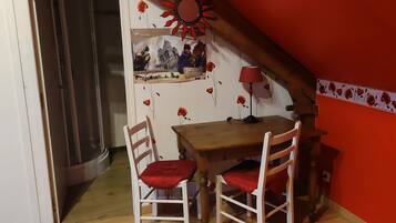A small dining area with a wooden table and two chairs, a red lamp, and a wall decorated with red flowers and a vintage photo.