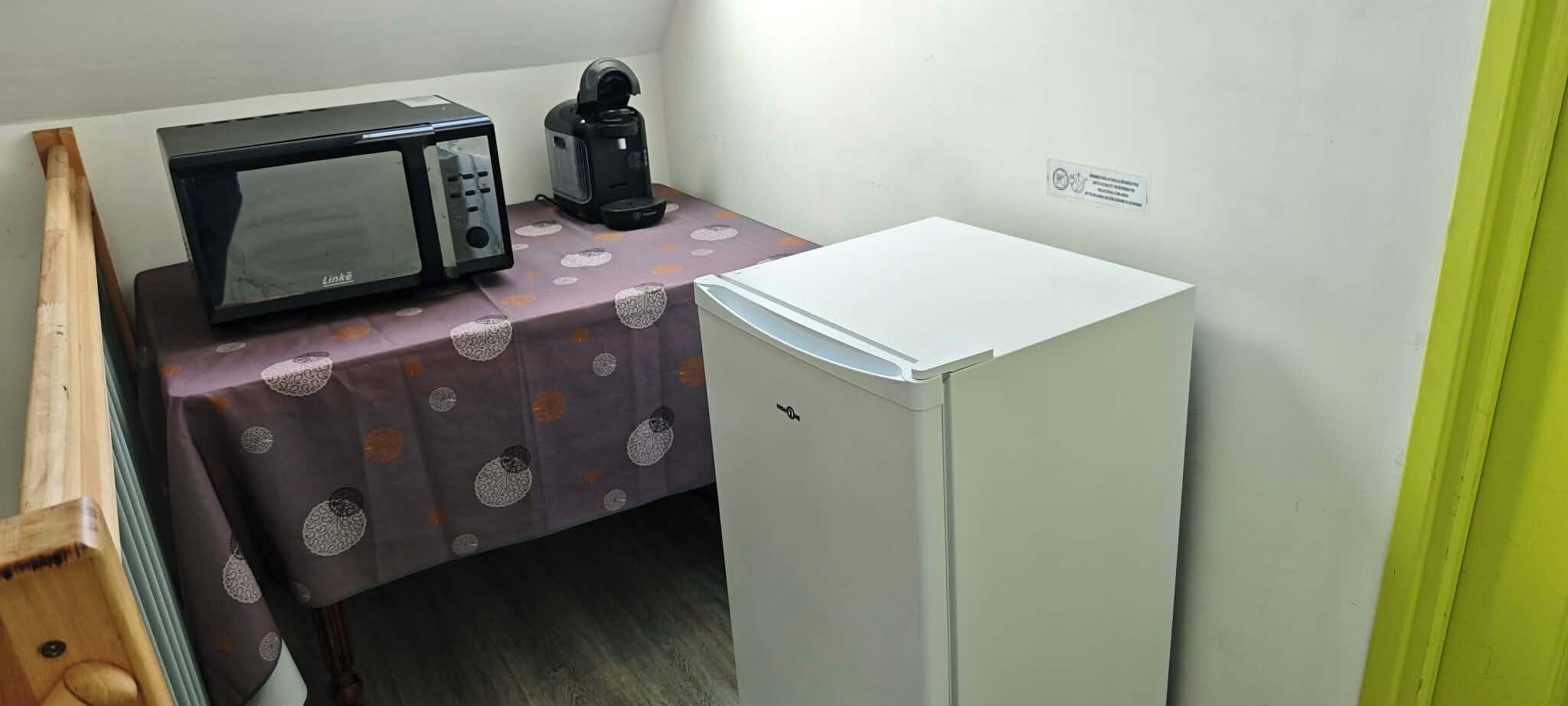Eine kleine Küchenzeile mit Mikrowelle, Kaffeemaschine und Kühlschrank.