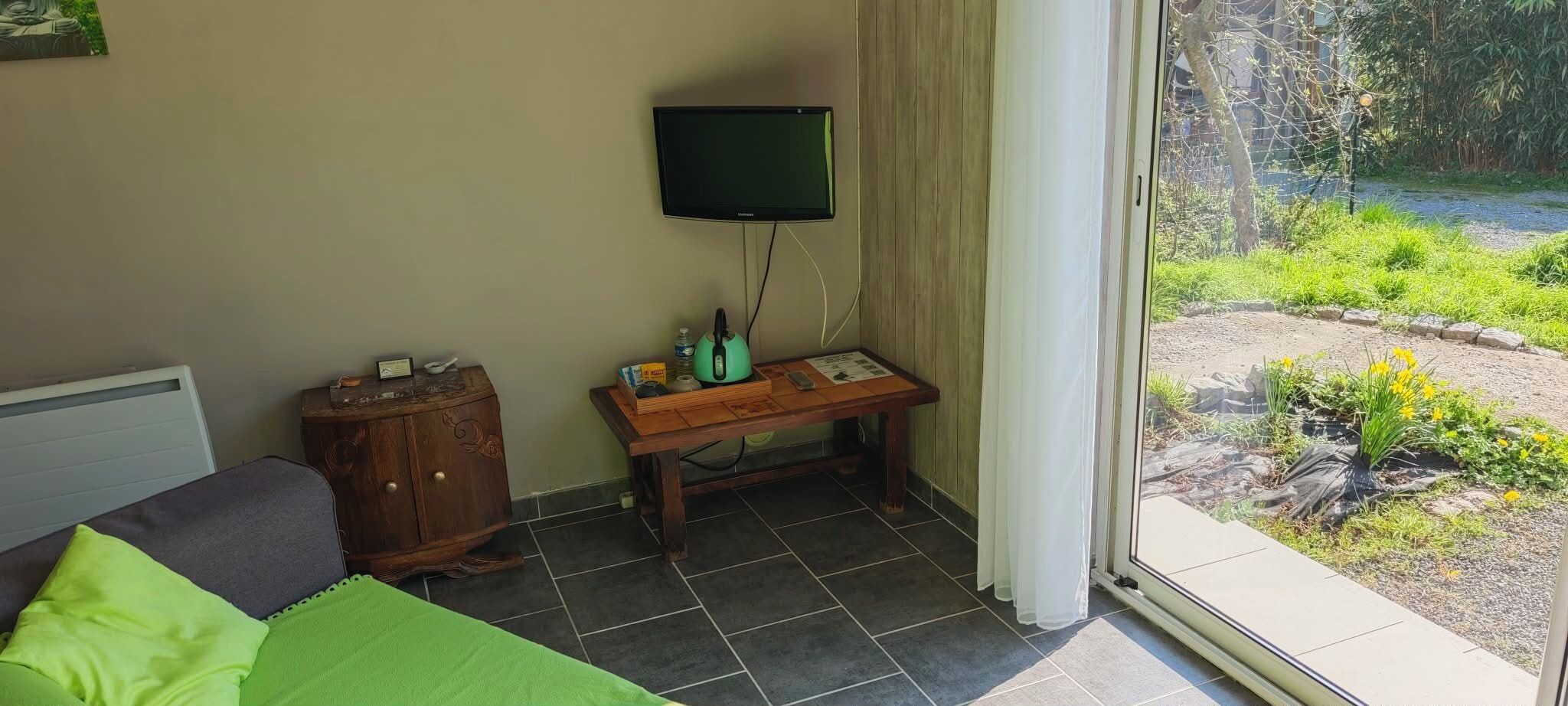 Een slaapkamer met een bed, een houten kast, een tafel met een televisie en uitzicht op een tuin.