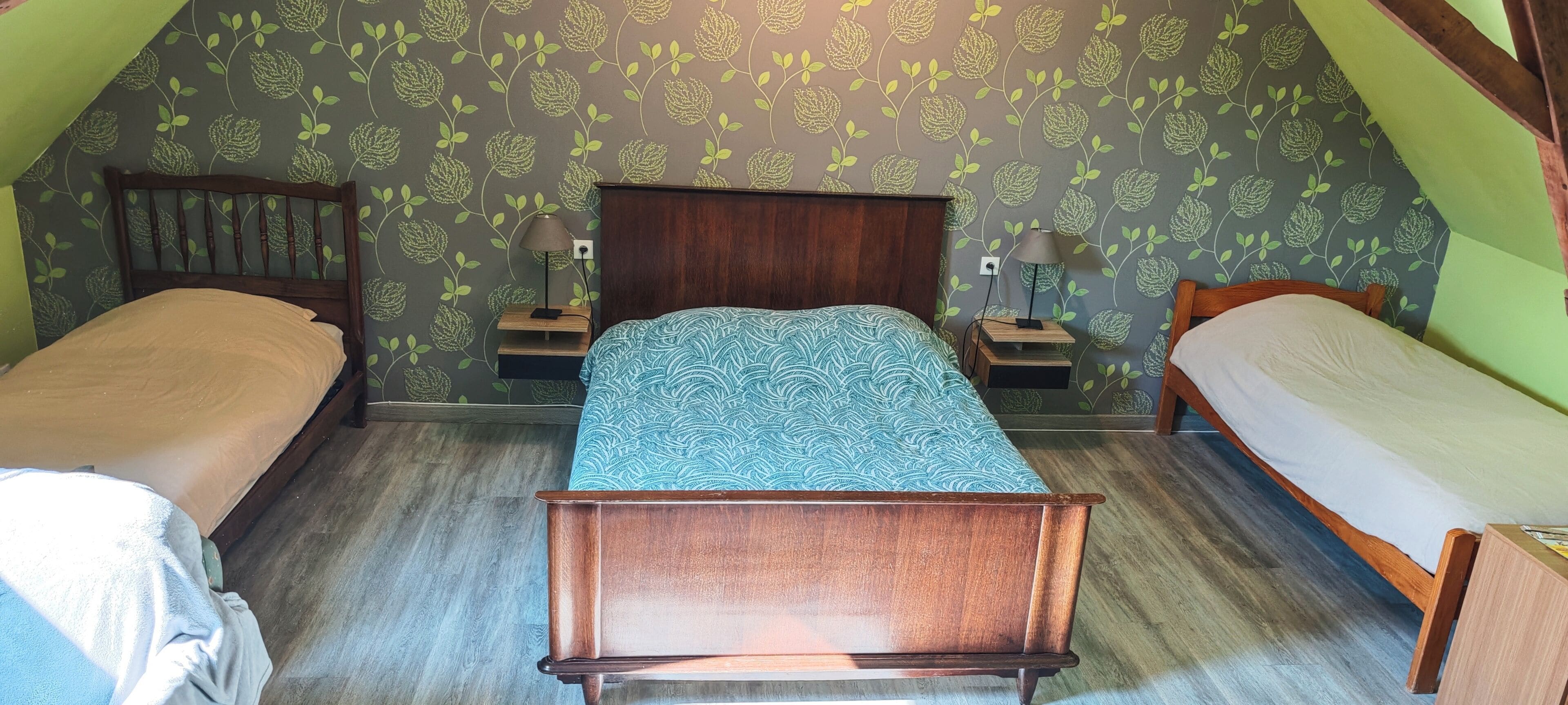 Een kamer met een schuine kap, twee eenpersoonsbedden, een centraal bed, houten hoofdborden en behang met een patroon.