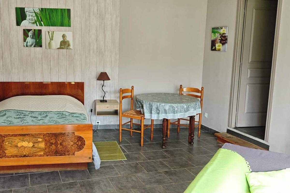 A bedroom with a wooden bed, a small table with chairs, a nightstand, and a wall-mounted lamp.