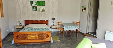 Un dormitorio con una cama de madera, una pequeña mesa con sillas, una mesita de noche y una lámpara de pared.