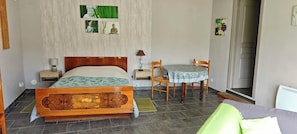 A bedroom with a wooden bed, a small table with chairs, a nightstand, and a wall-mounted lamp. - Les Chambres du Relais (Liettres)