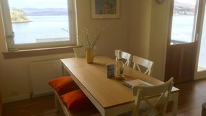 A dining area with a wooden table, white chairs, and a view of a body of water through large windows.
