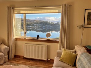 A room with a large window overlooking a lake, a radiator, a sofa, and a lamp. - Lovely sea and mountain views, spacious Portree home (Portree)