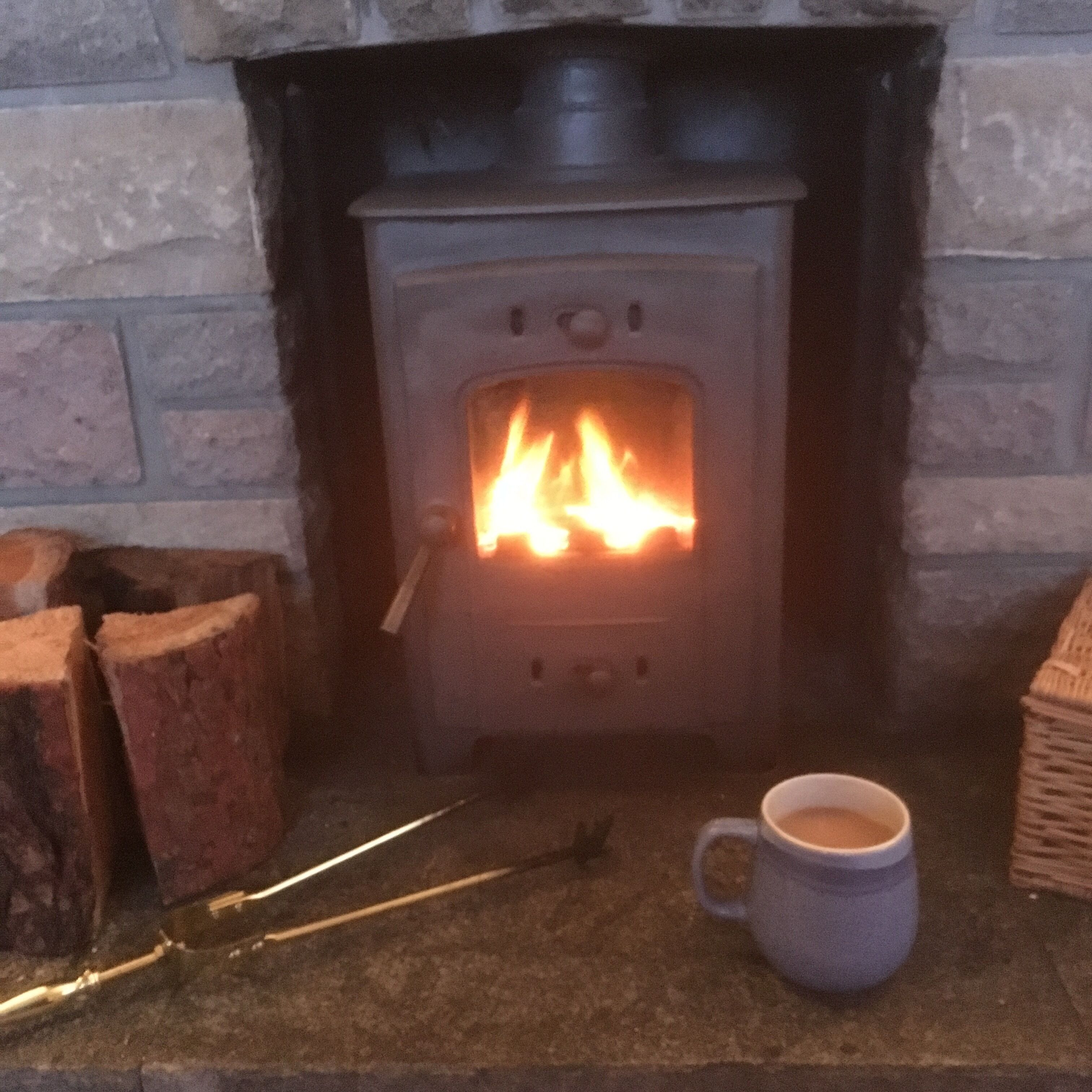 A fireplace with a visible fire, a cup of coffee on the mantel, and a brick wall.