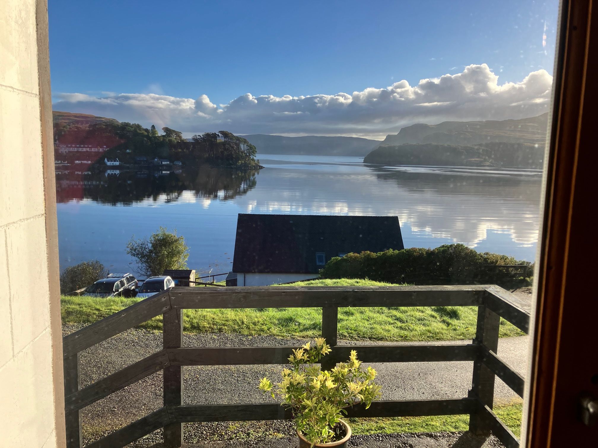 Une vue depuis un balcon doté d’une balustrade, donnant sur un lac paisible, avec une terre lointaine à l’horizon et un ciel dégagé.
