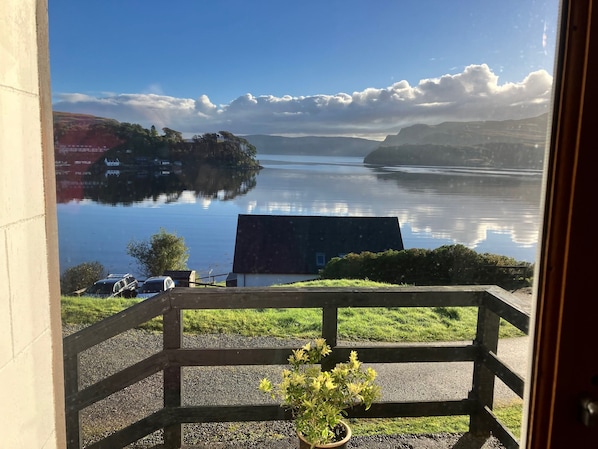 A view from a balcony with a railing, overlooking a calm lake with distant land and a clear sky. - Lovely sea and mountain views, spacious Portree home (Portree)