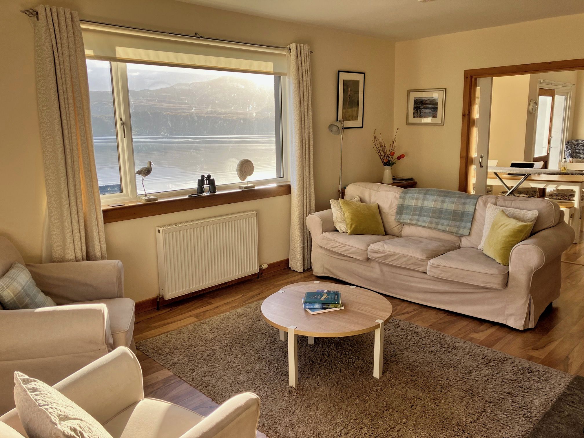 A living room with a sofa, armchairs, a coffee table, and a view of the sea through a large window.
