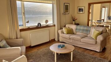 Un salon comprenant un canapé, des fauteuils, une table basse et une vue sur la mer, visible à travers une grande fenêtre.