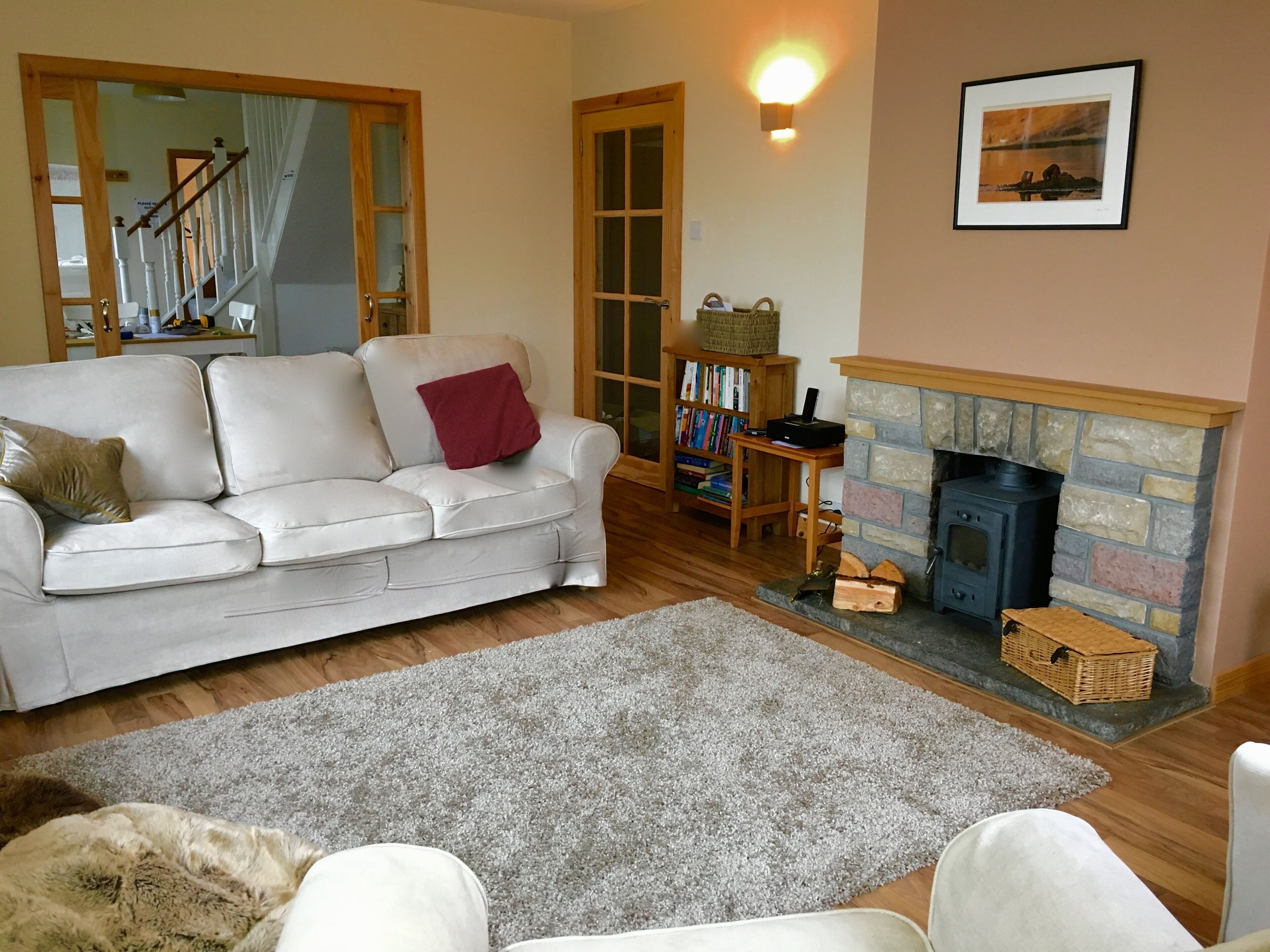 A cozy living room with a white sofa, a fireplace, a bookshelf, and a large mirror.