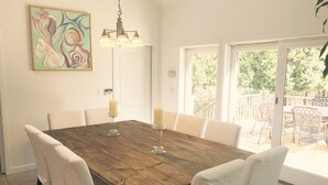 A dining area with a wooden table, white chairs, a chandelier, and a painting on the wall. - 6 Bedroom, 5 Bath Home with Pool, Sag Harbor - Near Bridgehampton (Sag Harbor)