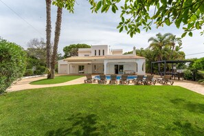A white villa with a swimming pool, outdoor seating, and a garden.