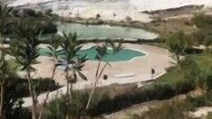 Un paisaje con zona de piscina rodeada de follaje y una gran formación rocosa.