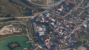 Vista aérea de un pueblo con una plaza central, edificios circundantes y una masa de agua con una pequeña isla.
