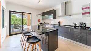 A modern kitchen with a central island, dark cabinetry, and a view to an outdoor patio. - Casa no Sol | 3 Bedrooms | Modern | Almancil (Almancil)
