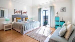 A bedroom with a bed, nightstands, a sofa, a large window with curtains, and a view of the outdoors. - Casa no Sol | 3 Bedrooms | Modern | Almancil (Almancil)
