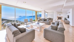 Uma sala de estar espaçosa com uma grande janela que oferece vista para o mar e as colinas.