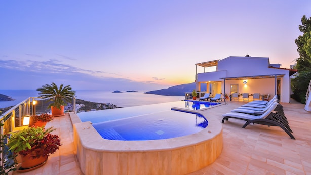Uma piscina infinita moderna com vista para o mar, área de estar coberta ao ar livre e plantas em vasos.