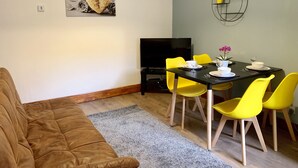 Un comedor con una mesa para dos, sillas amarillas, mantel negro y una pequeña planta en maceta en la pared.