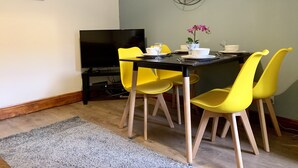 Un comedor con una mesa negra, sillas amarillas, un televisor y una planta en la pared.