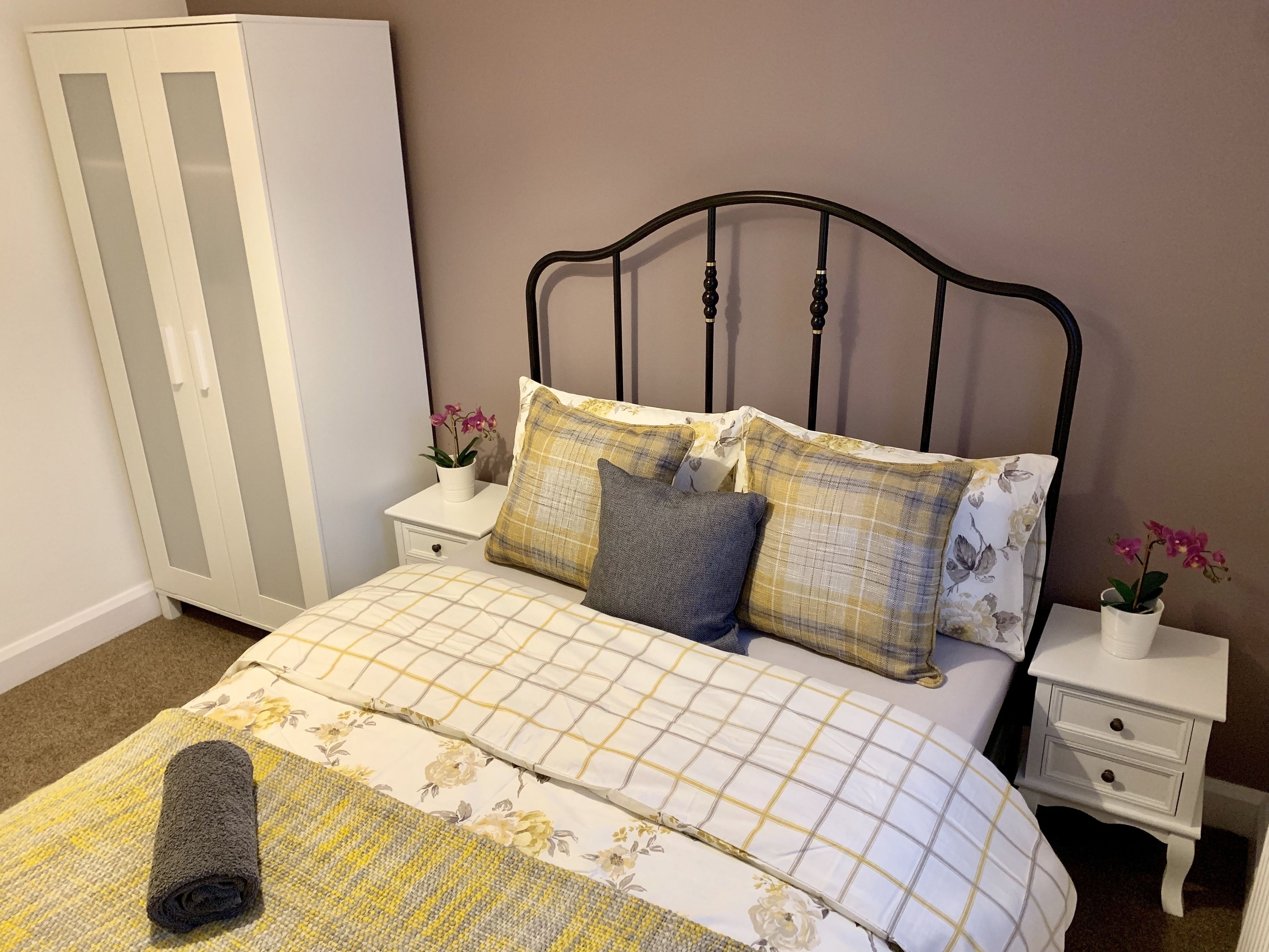 A bedroom with a bed, two nightstands, a wardrobe, and a rolled towel on the bed.
