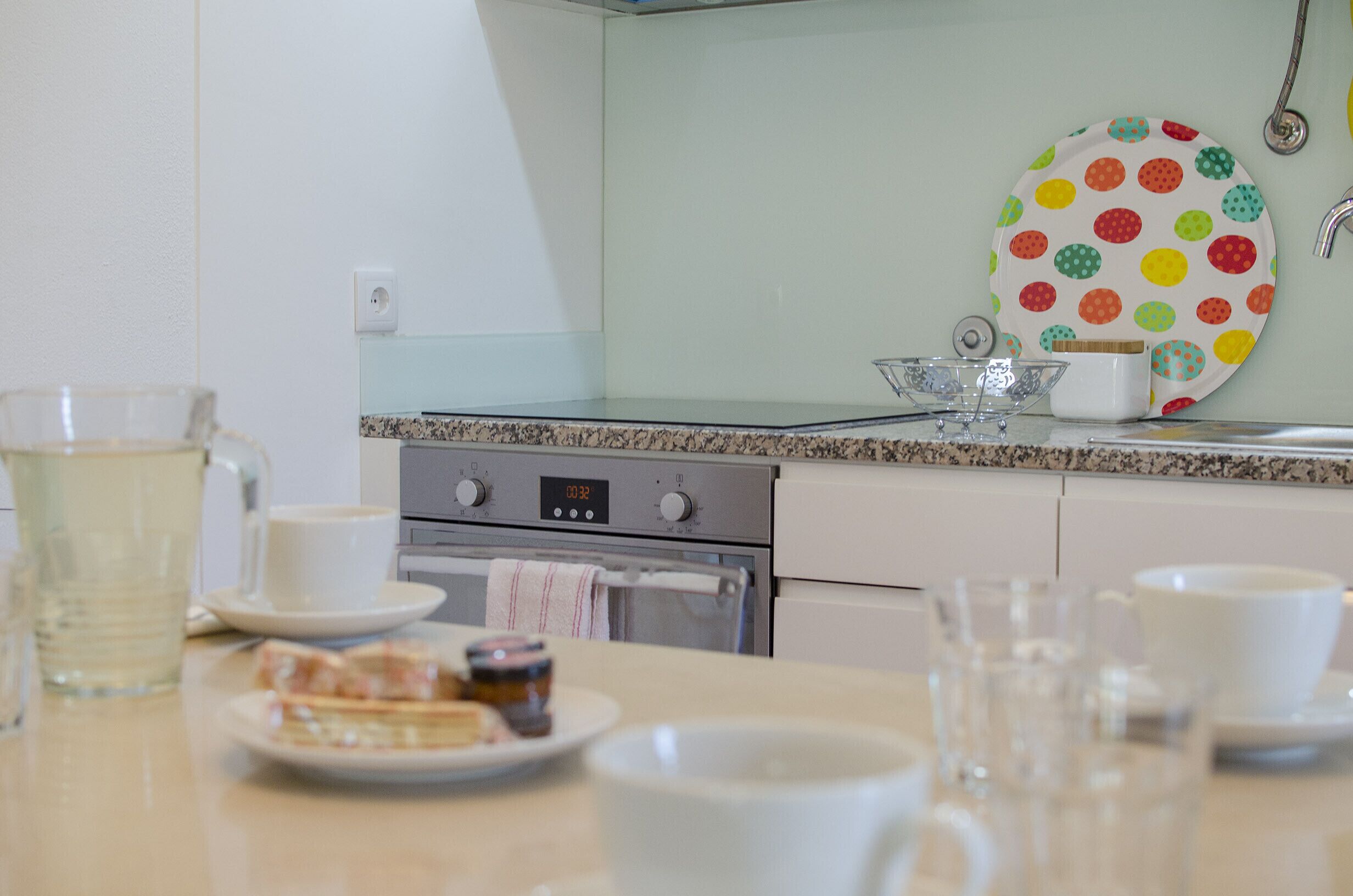 Een keuken met een aanrecht, een fornuis en een wandbord met kleurrijke stippen.