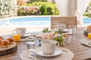 Ein Frühstückstisch mit Blick auf den Pool, bestückt mit Speisen, Tassen und Gläsern.