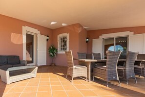 A sunlit patio with wicker furniture, a potted plant, and a view through a window. - Villa Anita | 5 Bedrooms | Private | Vilamoura (Vilamoura)