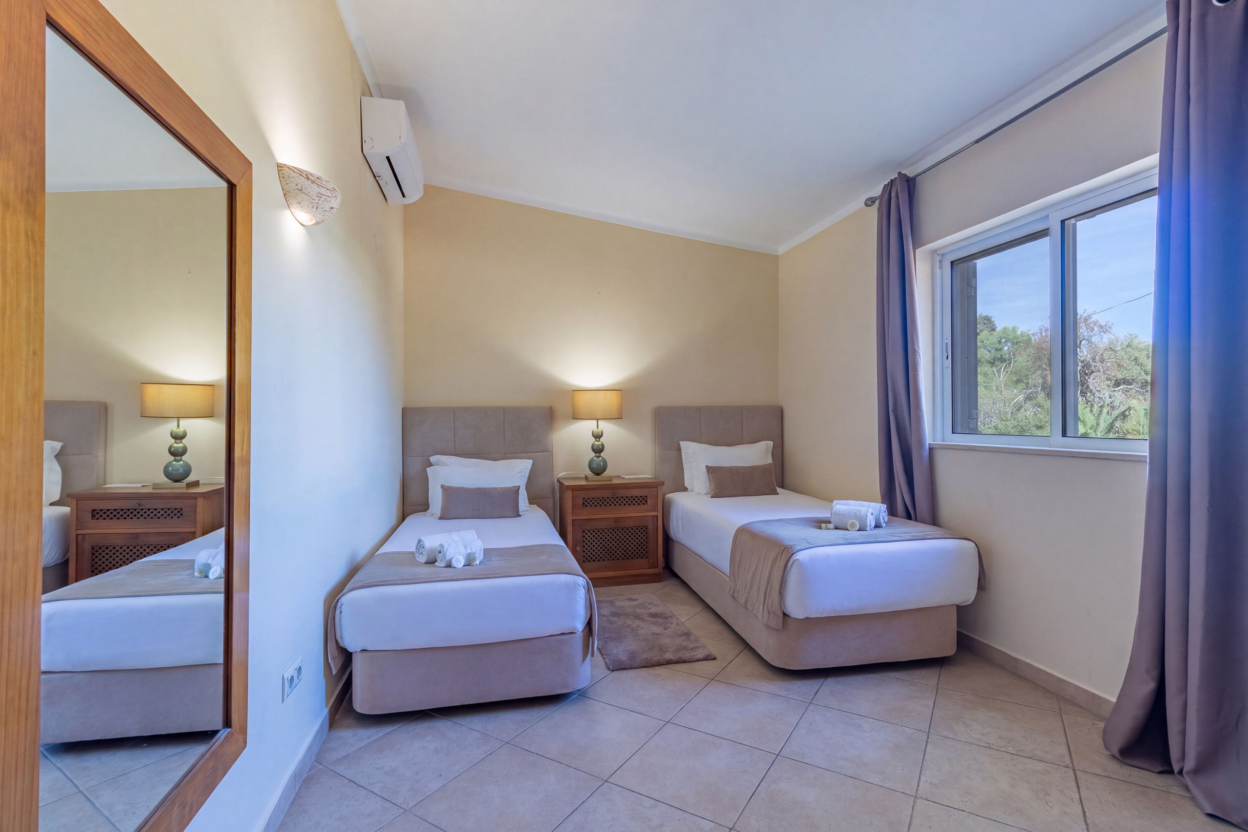 Une chambre d’hôtel avec deux lits simples, un grand miroir, une fenêtre avec des rideaux et un ventilateur de plafond.