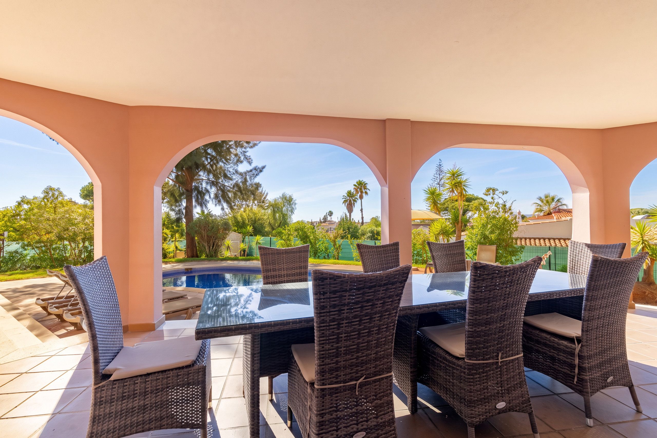 Un espace extérieur abrité, aménagé pour les repas, avec vue sur la piscine, doté de mobilier en osier et offrant un ciel dégagé.
